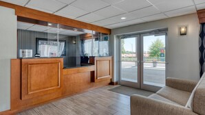 A reception area with a wooden reception desk, a glass partition, and a large sliding glass door leading outside. - SureStay Hotel by Best Western Bowling Green North (Bowling Green)