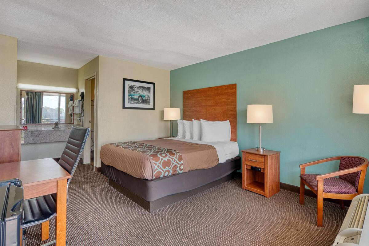 A hotel room with a bed, bedside tables, a chair, a desk, and a view of the outside.