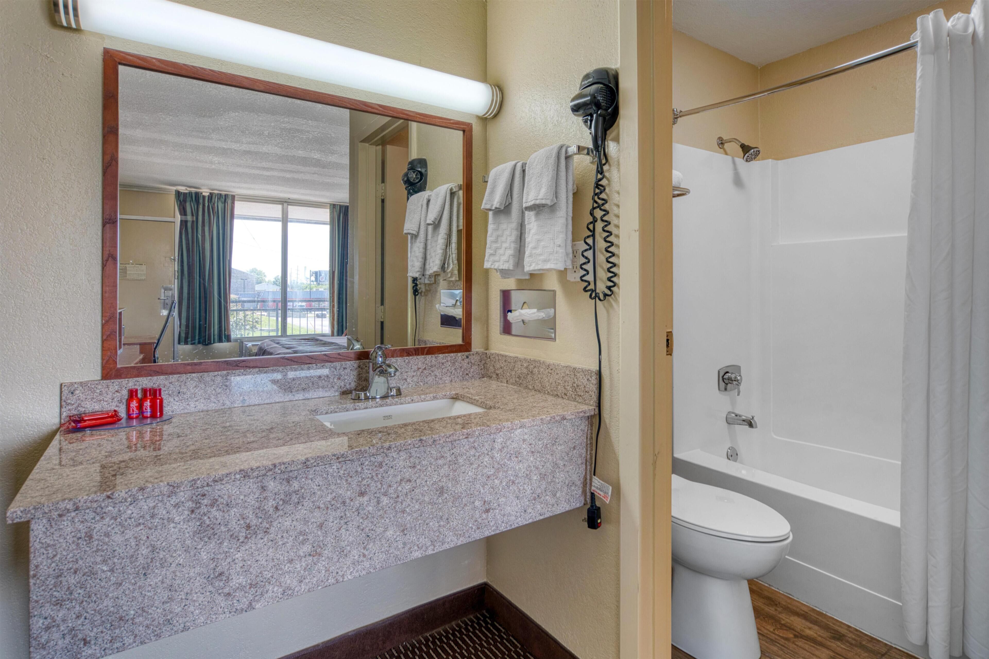 A bathroom with a sink, mirror, hairdryer, and shower.