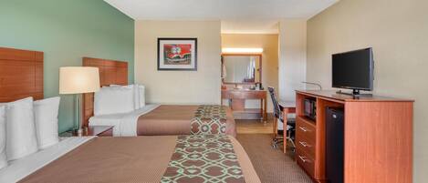A hotel room with two beds, a desk, a television, a mirror, and a bathroom visible in the background.