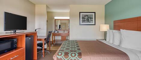 Een hotelkamer met een bed, bureau, televisie, koelkast en een schilderij aan de muur.