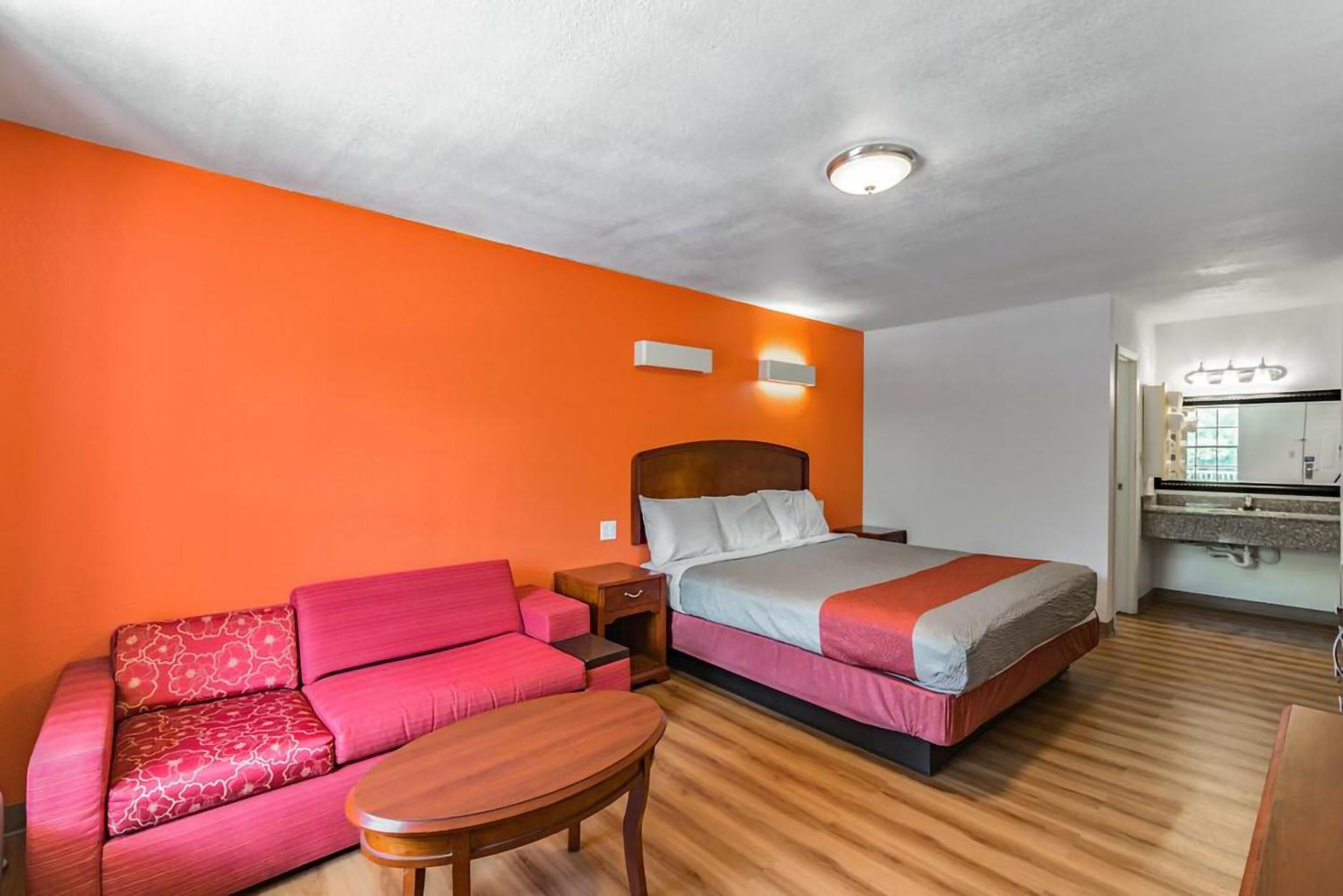 Camera d'albergo con un letto, un divano, un tavolino e un bagno con uno specchio e un lavandino.