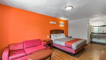 Camera d'albergo con un letto, un divano, un tavolino e un bagno con uno specchio e un lavandino.
