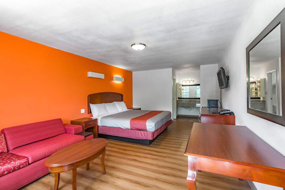 A hotel room with a bed, a red sofa, a wooden table, and a large mirror.