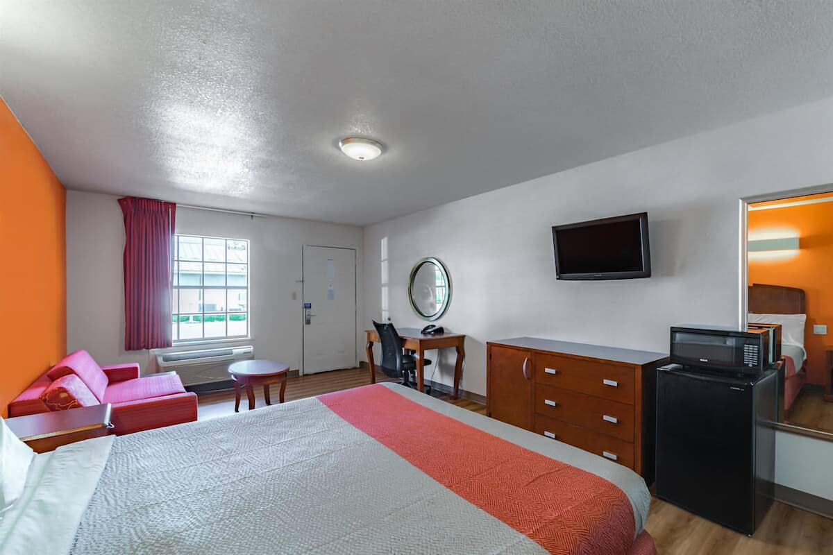A hotel room with a bed, a desk, a TV, a mirror, a dresser, and a microwave.
