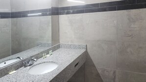 Un baño con encimera de granito, lavabo, espejo y pared revestida de baldosas negras.