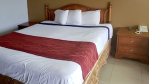 Una cama bien hecha con ropa de cama blanca y roja, un cabecero de madera y una mesita de noche con un teléfono y un objeto pequeño encima.