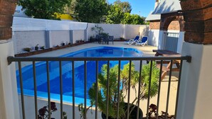 Une piscine entourée d’une rambarde en métal, agrémentée de plantes en pot et d’un espace patio avec des chaises et une table.