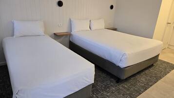 A hotel room with two single beds, a small wooden nightstand, a wall-mounted light, and a door.