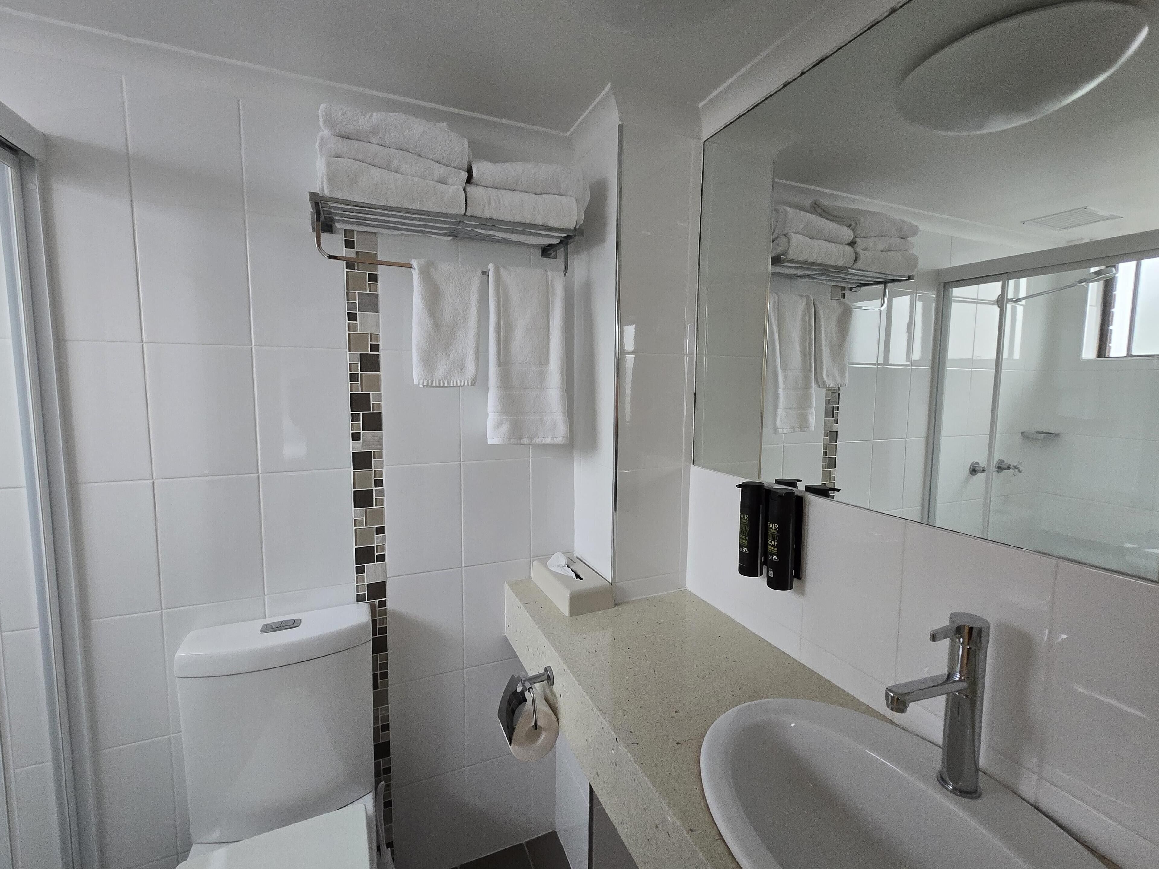 A modern bathroom with a toilet, sink, and shower. There are towels hanging on a rack and a mirror above the sink.