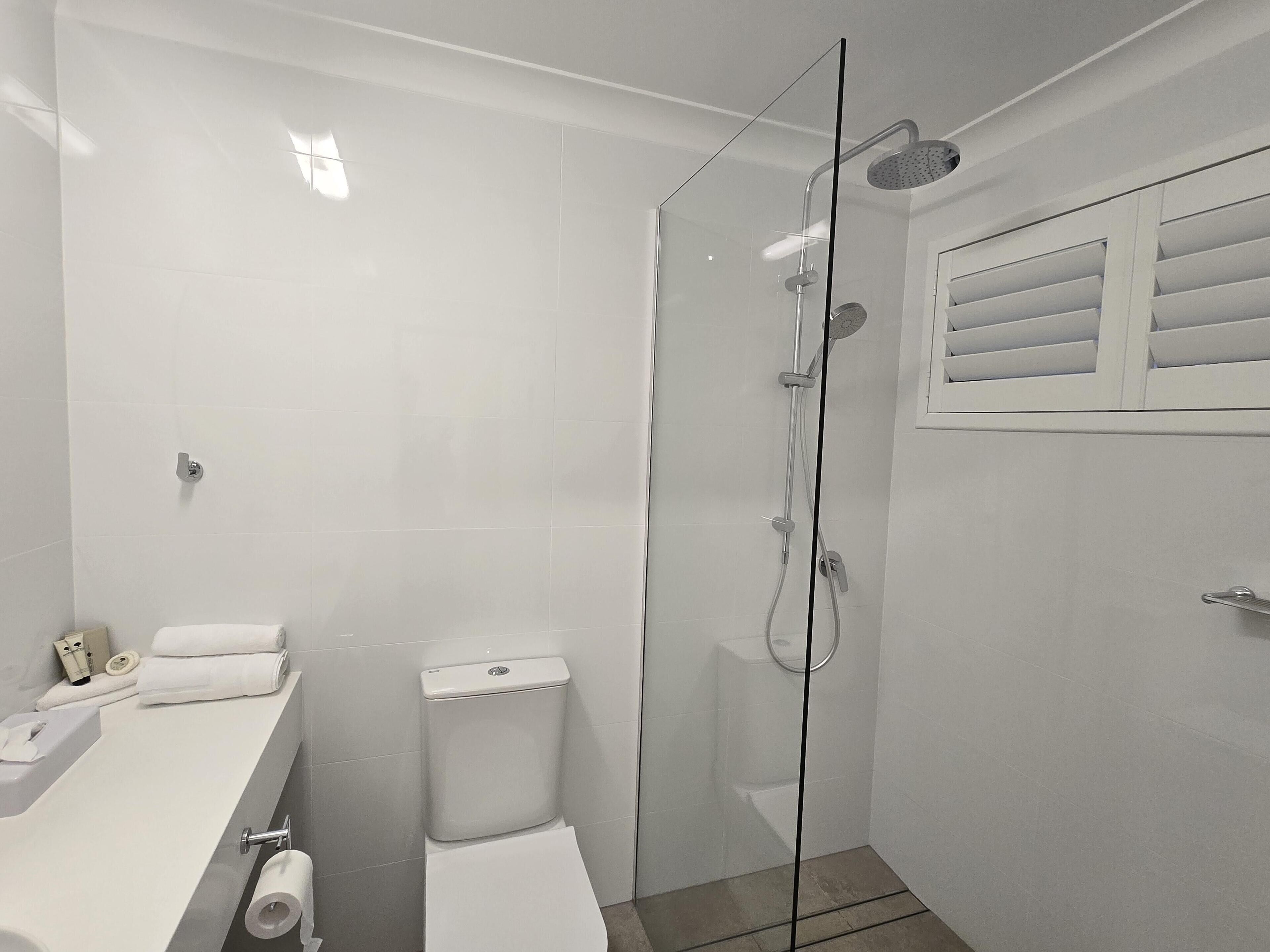 A modern bathroom with a glass-enclosed shower, white tiles, a toilet, and a sink with toiletries.
