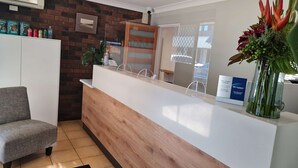 Un espace d’accueil avec un comptoir en bois, un tableau encadré au mur et un panneau indiquant les engagements de service.