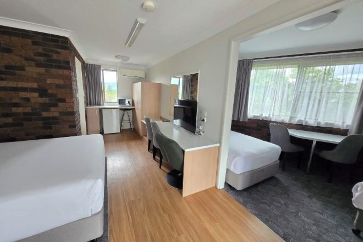 A hotel room with two single beds, a desk with a chair, a television, and a window with curtains.