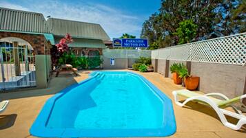Ein Swimmingpool mit blauer Umrandung, umgeben von einem weißen Zaun, und ein Schild für 'Parkside Motor Inn' im Hintergrund.