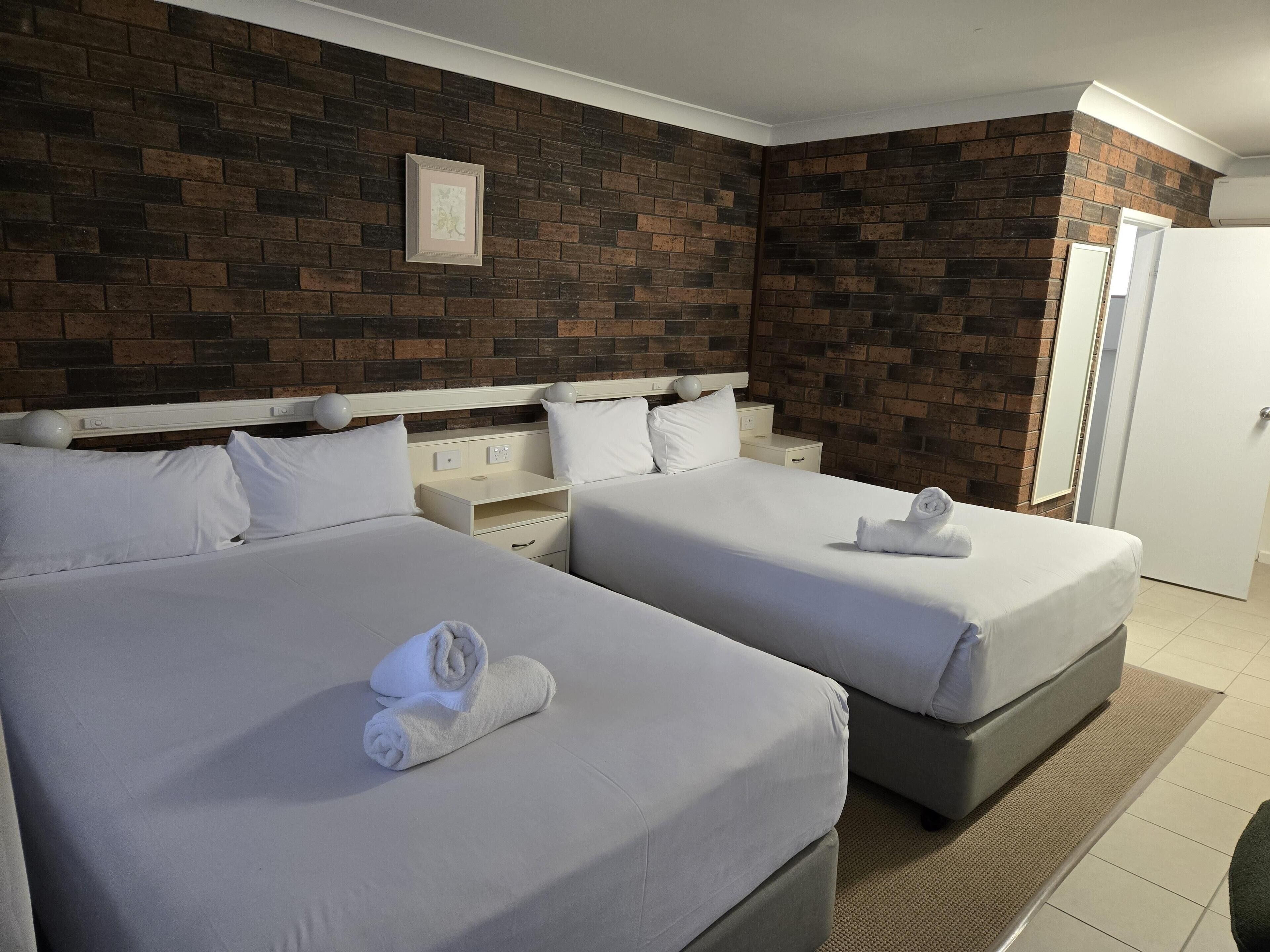 Une chambre d’hôtel avec deux lits, un mur en briques, un tableau encadré et une porte blanche.