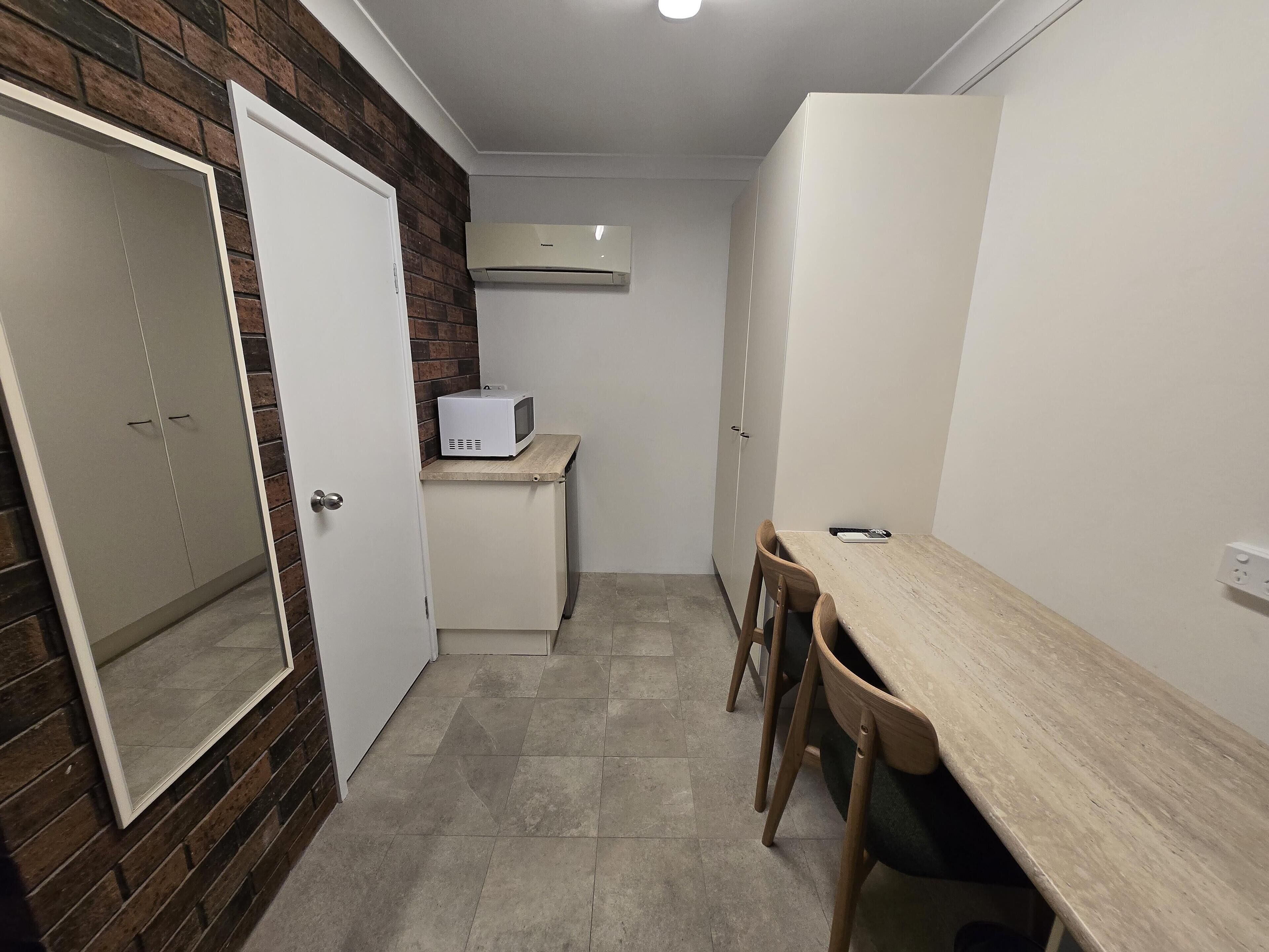 Et kompakt køkken med en mikrobølgeovn på en lille bordplade, et spisebord med stole og en garderobe med spejl.