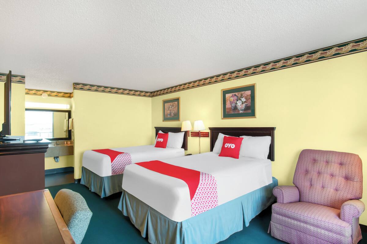 A hotel room with two beds, a desk, a chair, and a mirror.