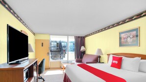 A hotel room with a bed, a TV, a desk, a chair, a window with a view of a balcony, and a painting on the wall. - OYO Hotel Oklahoma City South I-35 and SE 29th (Oklahoma City)
