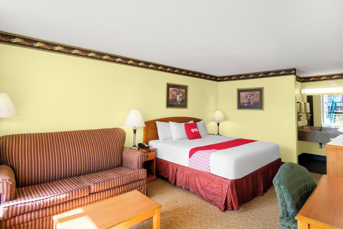 A hotel room with a bed, a striped sofa, a desk, and a chair.