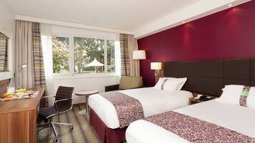 A hotel room with two beds, a desk with breakfast, a chair, and a view of trees through the window.