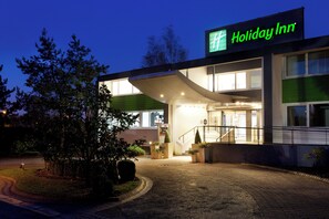 A Holiday Inn hotel entrance with a covered outdoor area, a staircase, and a paved driveway. - Holiday Inn Lille - Ouest Englos by IHG (Englos)