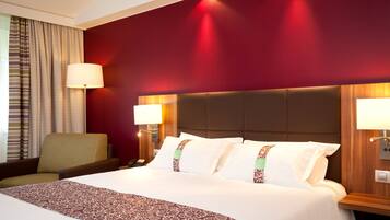A hotel room with a large bed, a chair, a desk, and a lamp.