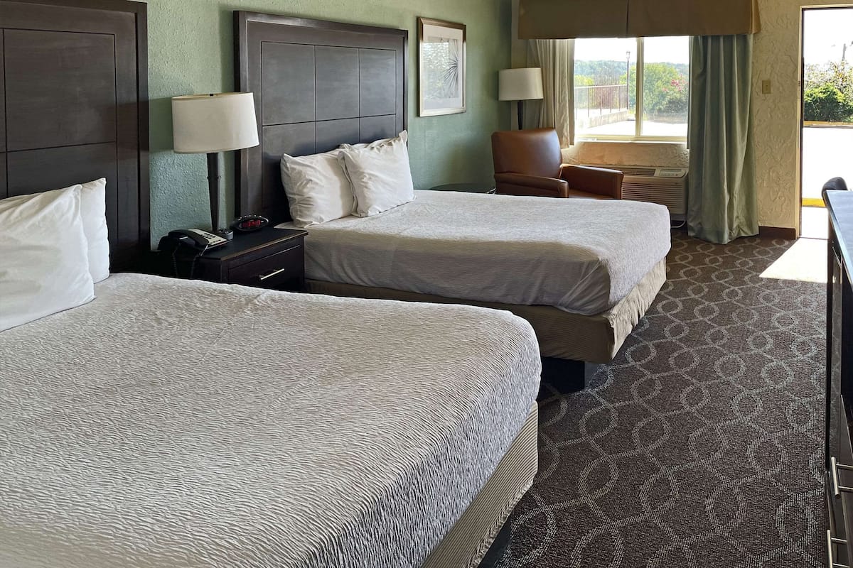 A hotel room with two beds, a desk, a chair, and a window with curtains.