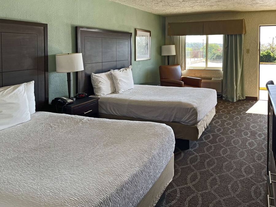 Habitación de hotel con dos camas, un escritorio, una silla y una ventana con cortinas.