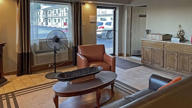 A hotel room with a leather sofa, a small round table, a standing fan, and a view of the street through a large window. - Quality Inn Clinton North (Clinton)