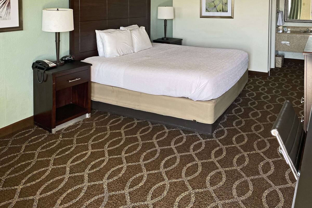 A hotel room with a large bed, two bedside tables with lamps, a desk with a phone, a framed picture on the wall, and a bathroom visible through an open door.