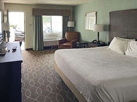 A hotel room with a large bed, a desk with a telephone, a chair, a small table, and a window with curtains.