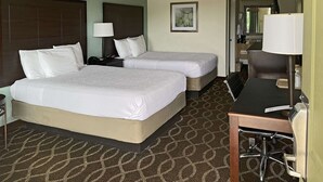 A hotel room with two beds, a desk, a chair, a lamp, a framed picture, and a bathroom visible through an open door.