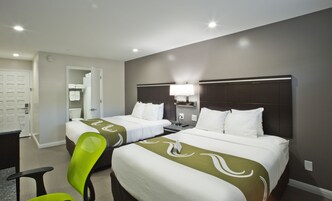 A hotel room with two beds, a desk, a chair, and a bathroom visible through an open door.