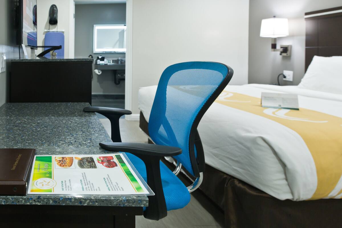 Habitación de hotel con cama, escritorio con un menú, una silla azul y un baño al fondo.