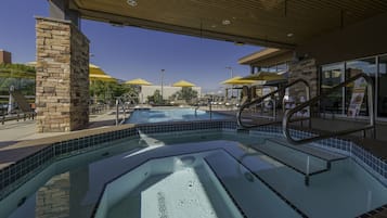 Una piscina con un pilar de piedra, bordes con mosaicos y estructura de techo de madera.