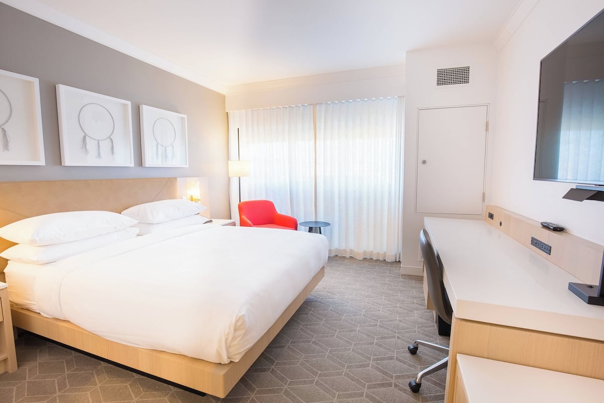 A hotel room with a large bed, a desk, a chair, and a TV.