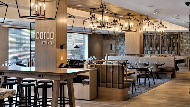Un restaurante moderno con barra, detalles de madera e iluminación colgante de estilo geométrico.