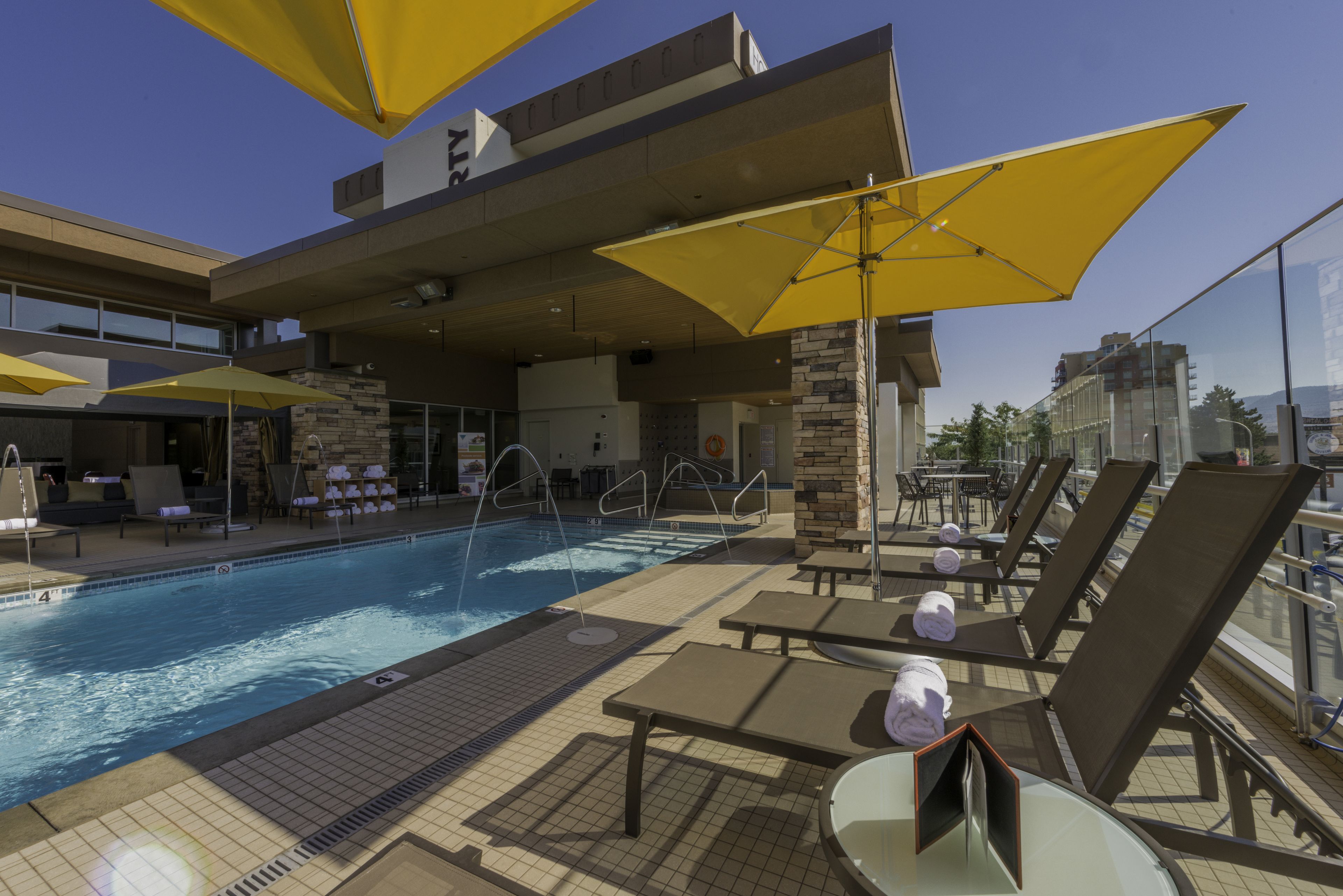 A rooftop pool area with lounge chairs, umbrellas, and a clear view of the city skyline.