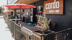 Un área de estar al aire libre con sombrillas rojas y un letrero que dice 'Cordo RESTO + BAR'.