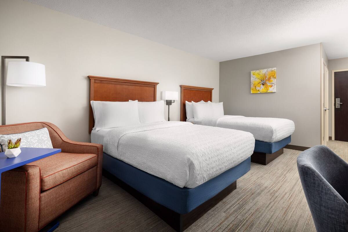 Habitación de hotel con dos camas, un escritorio, una silla y una lámpara.