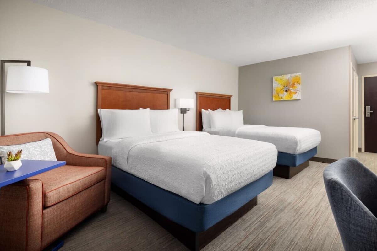A hotel room with two beds, a sofa, a desk, and a lamp.