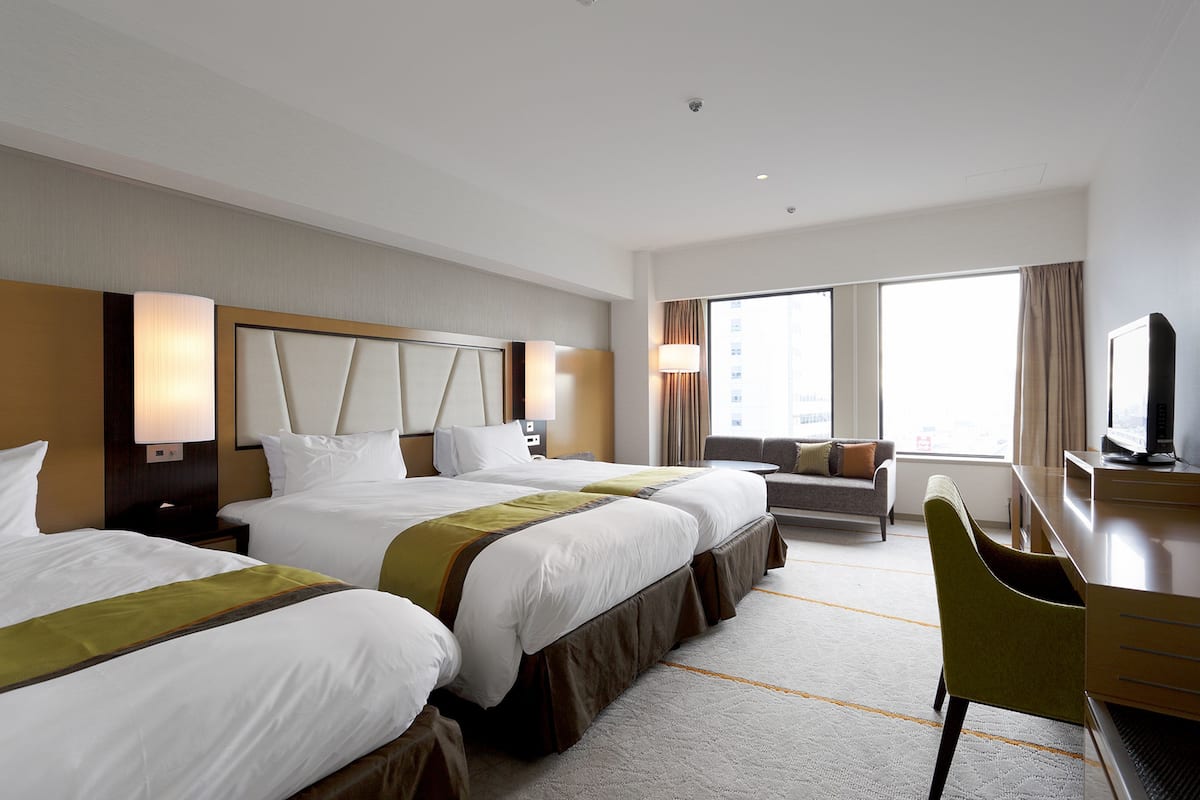 A hotel room with two beds, a desk, a chair, and a large window.