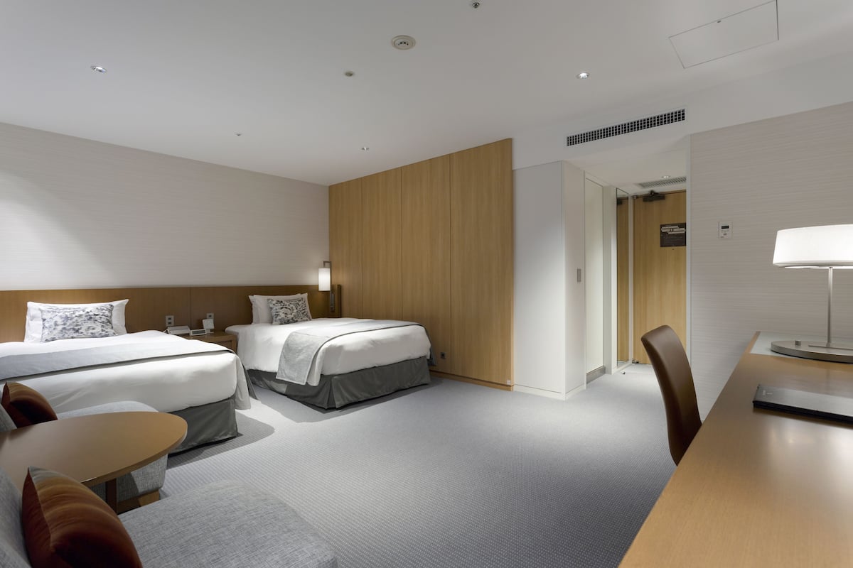 A modern hotel room with two beds, a desk, and a chair.