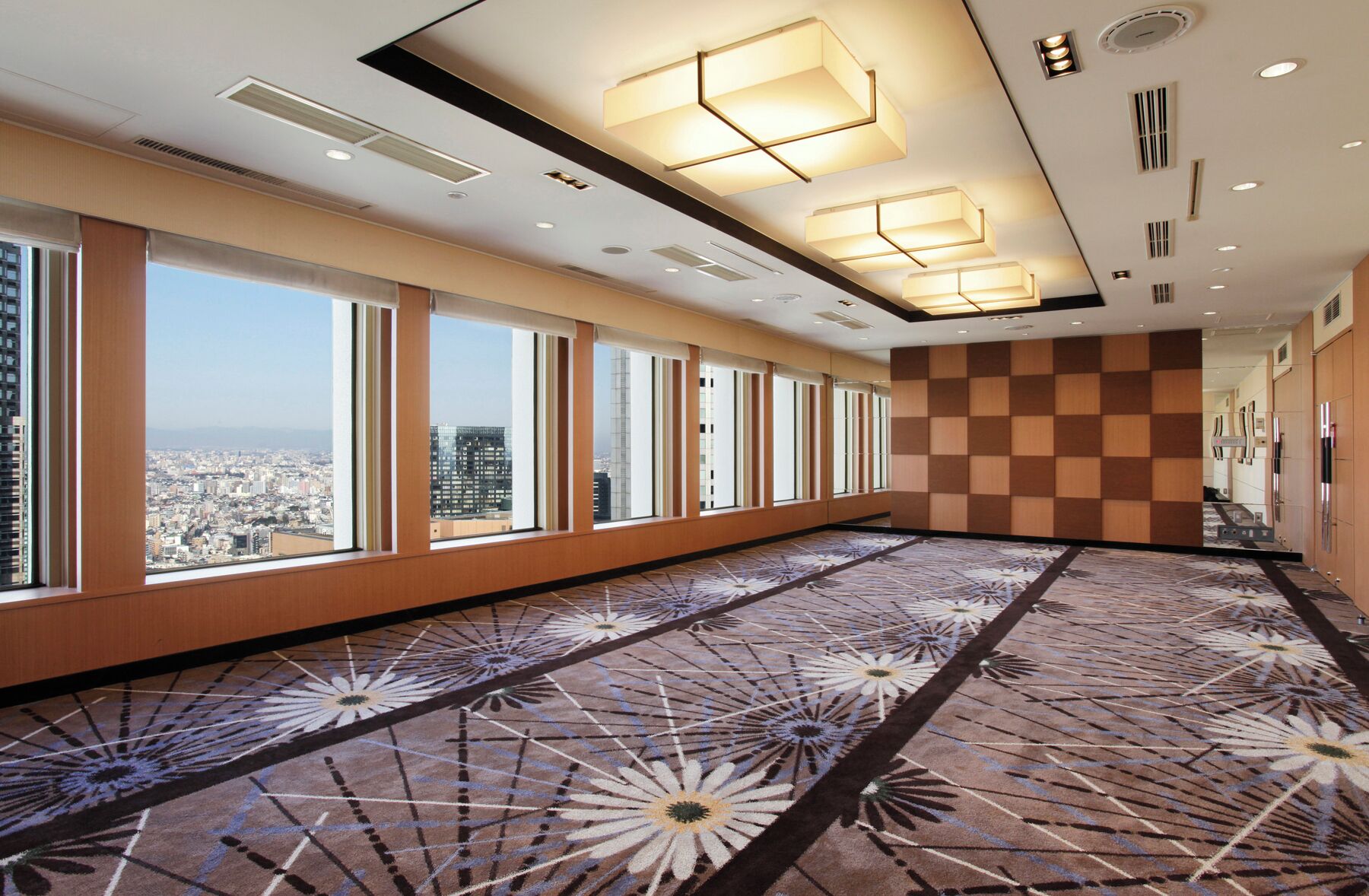 Un salón de conferencias de hotel con amplios ventanales, alfombra estampada e iluminación moderna.