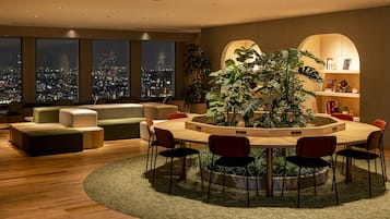 Un salon moderne avec une table ronde en bois, des chaises rouges, un canapé vert et une grande plante au centre.