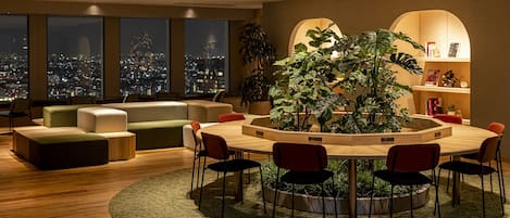 A modern living room with a round wooden table, red chairs, a green sofa, and a large plant in the center.