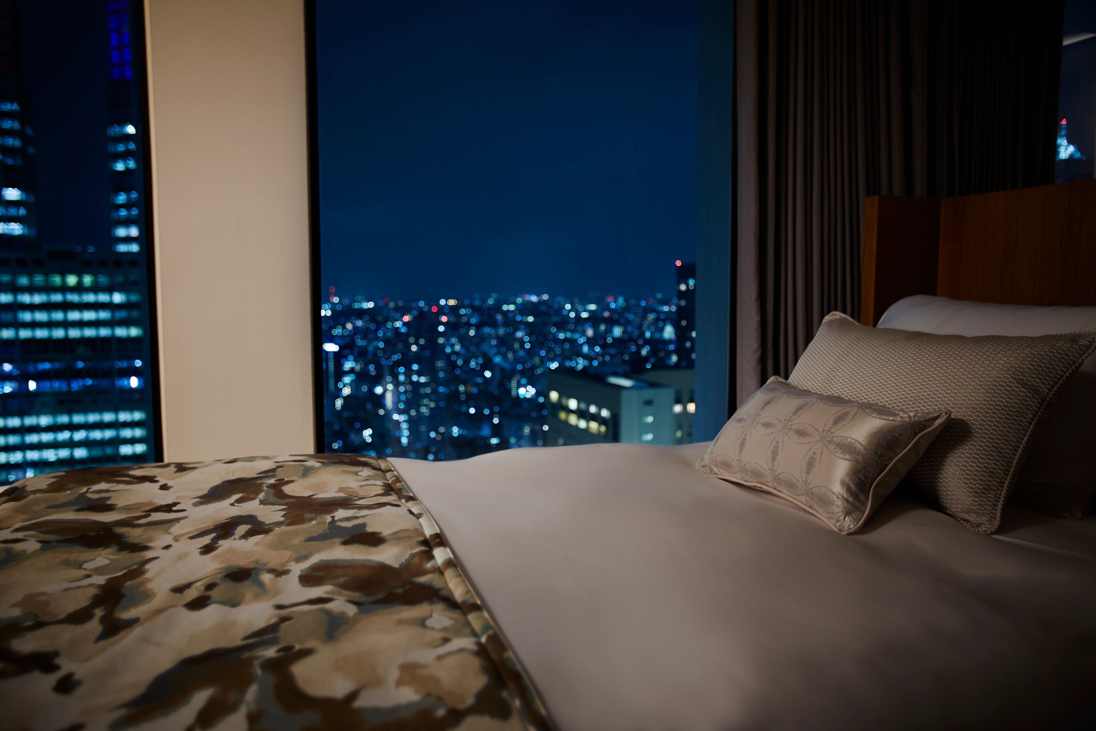 Habitación de hotel con cama, vista nocturna de la ciudad y ventana con cortinas.
