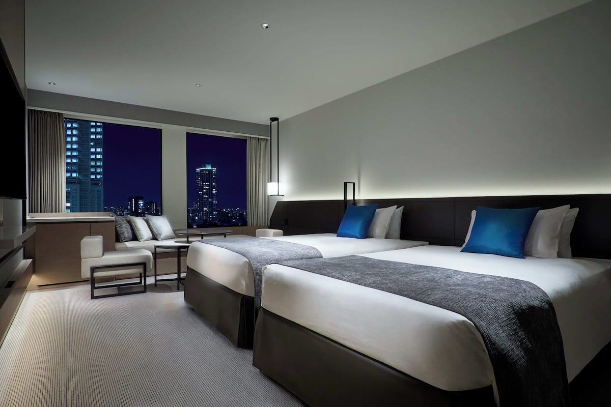 A hotel room with two beds, a sofa, a TV, and a city view.