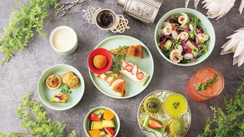 A variety of food items and drinks arranged on a table, including a salad, fruit, pastries, and a cocktail.