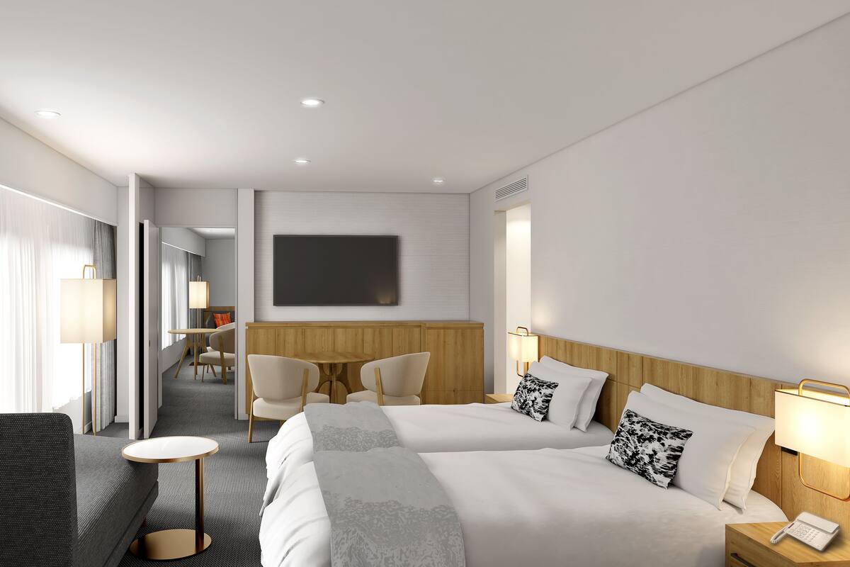 A hotel room with two beds, a desk, chairs, a TV, and a phone on the bedside table.